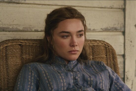 "A young woman in a blue patterned dress sits pensively in a wicker chair against a worn wooden wall, appearing thoughtful and somber in a rustic, vintage setting."